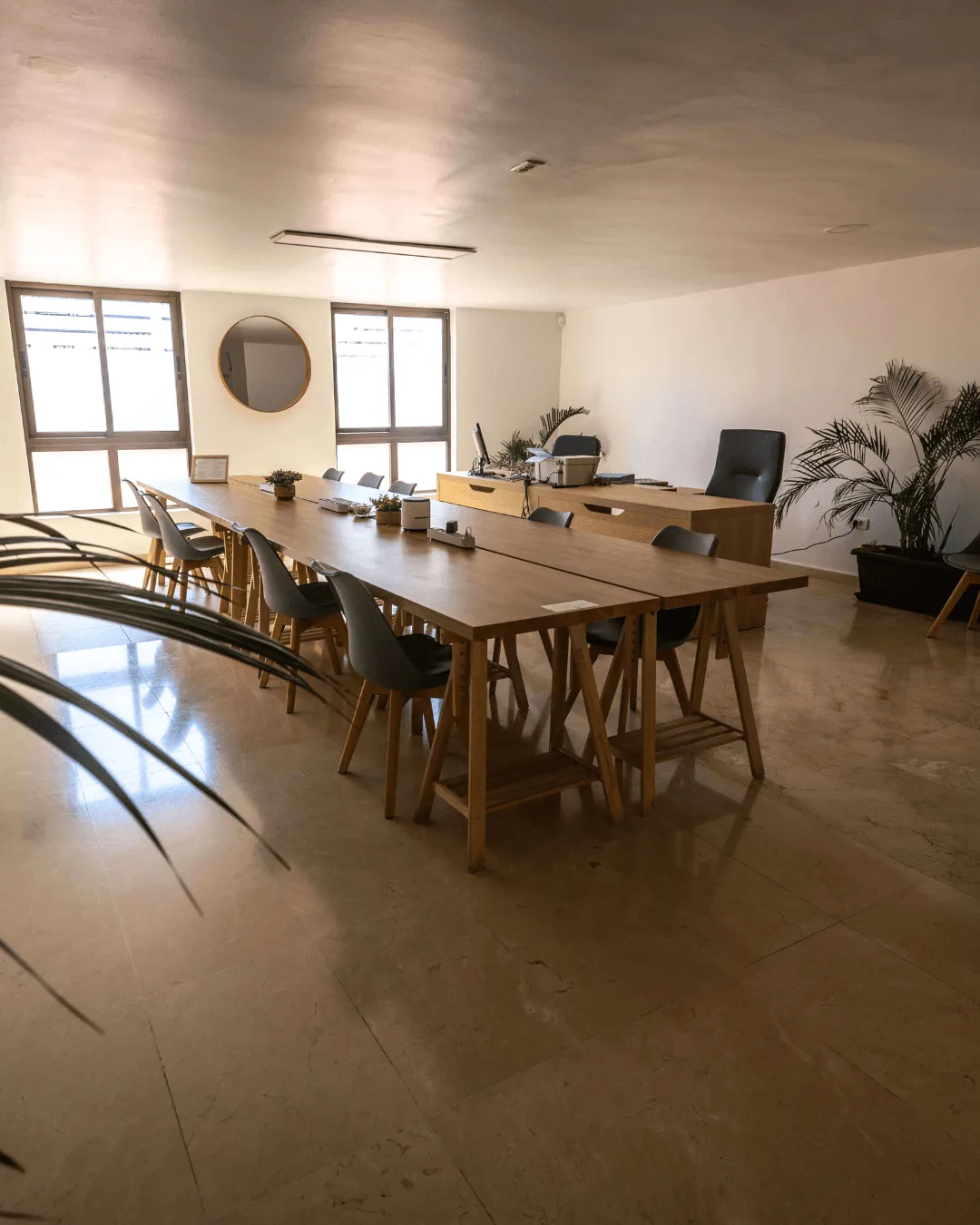 Raum im Coworking Mazaroco mit langen Holztischen, Stühlen und Pflanzen
